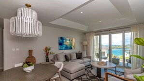 Una sala de estar moderna con sofá, mesa de comedor y sillas. Hay un ventanal con vista al mar.