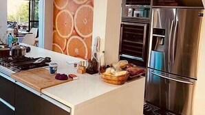 A modern kitchen with a central island, stainless steel appliances, and a large window providing natural light. - Paradise House - Angra dos Reis (Conceição de Jacareí)