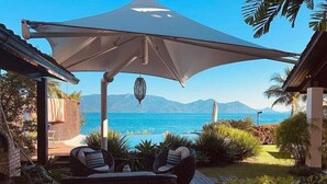 A patio with a large umbrella, wicker furniture, and a view of the sea and mountains. - Paradise House - Angra dos Reis (Conceição de Jacareí)