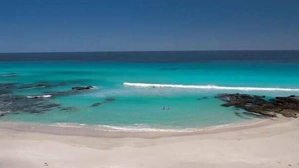 Une plage aux eaux turquoise et limpides, bordée de formations rocheuses.