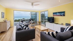 Un salon moderne avec vue sur l’océan, doté d’un ventilateur de plafond et d’un téléviseur posé sur un meuble.