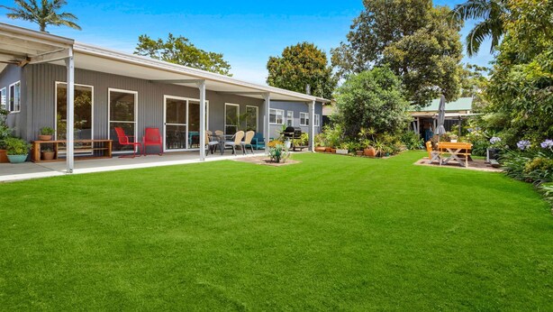 Ein modernes Haus mit einer überdachten Terrasse, einem gepflegten Rasen und verschiedenen Gartenmöbeln.