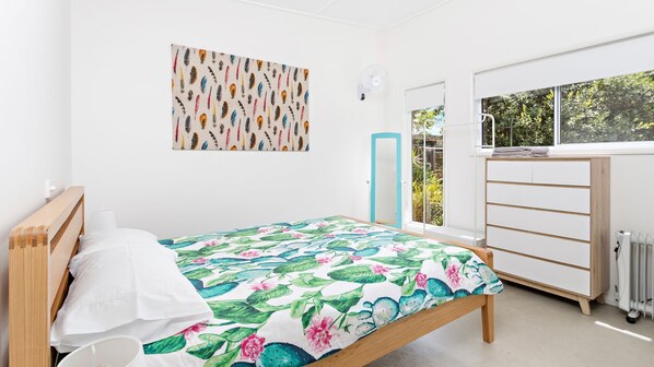 A bedroom with a bed, a dresser, a radiator, and a window with a view of greenery. - Sojourne - Perfect for 2 families (Shoalhaven Heads)