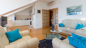 A modern living room with a glass coffee table, beige sofas with blue cushions, a kitchen in the background, and a painting on the wall. - Apartment  Bellissima vista (Dubrovnik)