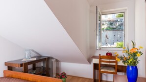 A bedroom with a bed, a wooden table, a chair, a radiator, a window with a view of the outside, and a vase with flowers. - Apartment  Bellissima vista (Dubrovnik)