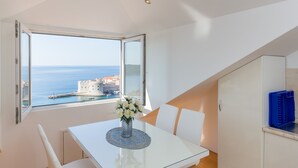 A dining area with a table, chairs, and a vase of flowers. A large window offers a view of the sea and a distant building. - Apartment  Bellissima vista (Dubrovnik)