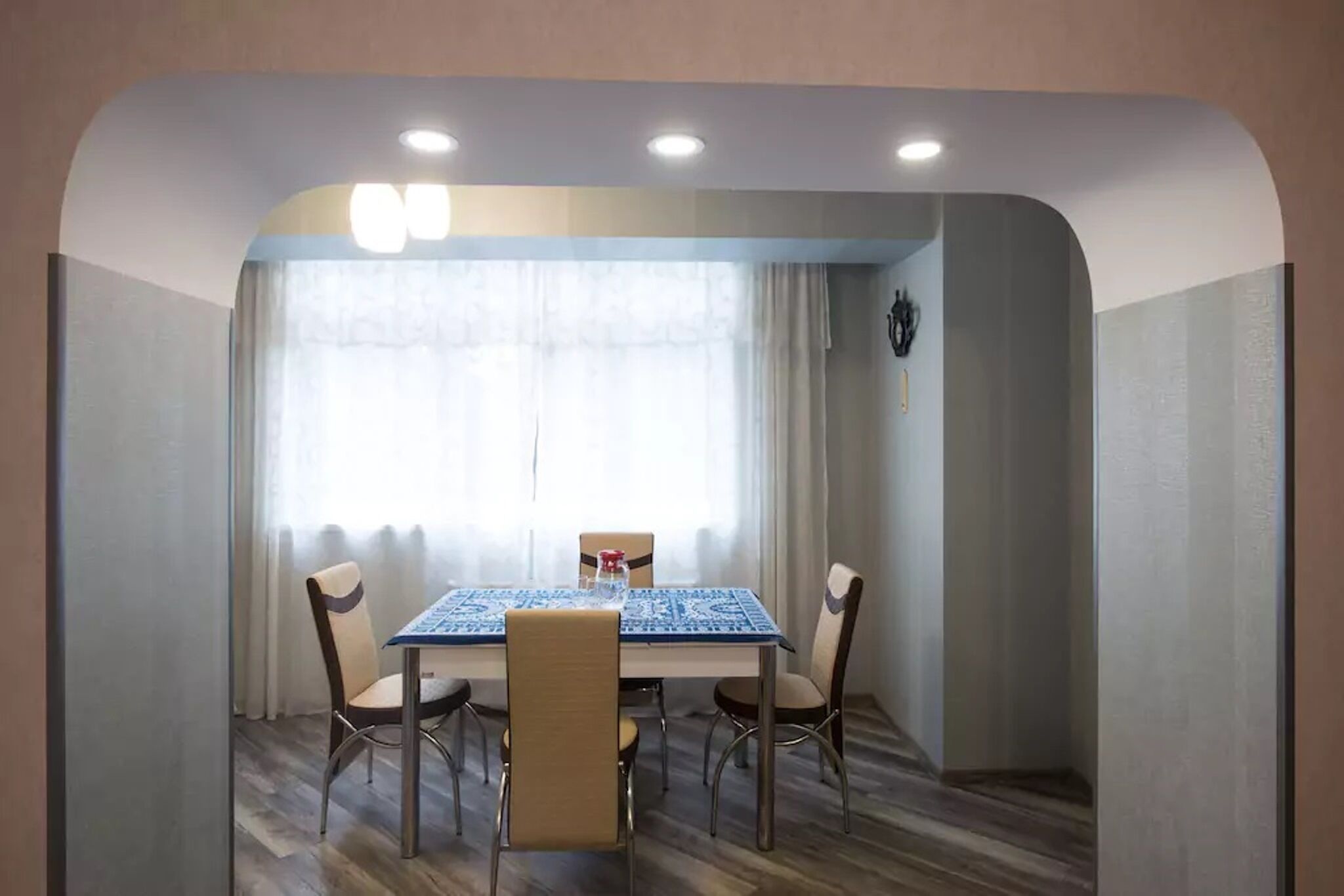 A dining area with a table and chairs, a window with curtains, and a clock on the wall.