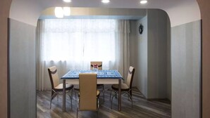 Een eethoek met een tafel en stoelen, een raam met gordijnen en een klok aan de muur.