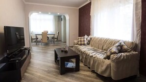 Een woonkamer met een bank, een salontafel en een televisie. Op de achtergrond is een eethoek te zien.