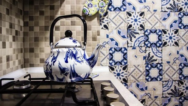 Een keuken met een gasfornuis, een blauw-wit theepot en betegelde muren.