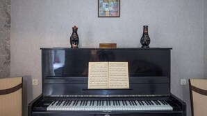 Een piano met bladmuziek ervoor, twee decoratieve vazen erop en een lijst met een schilderij aan de muur.