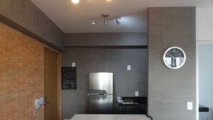 A modern kitchen with a stainless steel refrigerator, a clock on the wall, and a brick wall on one side. - Brand new, cozy apartment, close to the subway, fast Wi-Fi, Netflix.  (Pinheiros)
