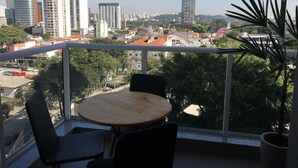 A balcony with a round table and two chairs, overlooking a cityscape with various buildings and a clear sky. - Brand new, cozy apartment, close to the subway, fast Wi-Fi, Netflix.  (Pinheiros)
