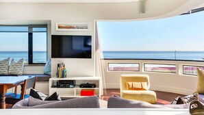 Una sala de estar moderna con un televisor grande, libros y vista al océano.