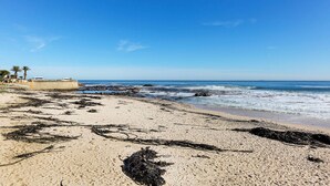 Una playa con cielos despejados, costa rocosa y vegetación escasa.