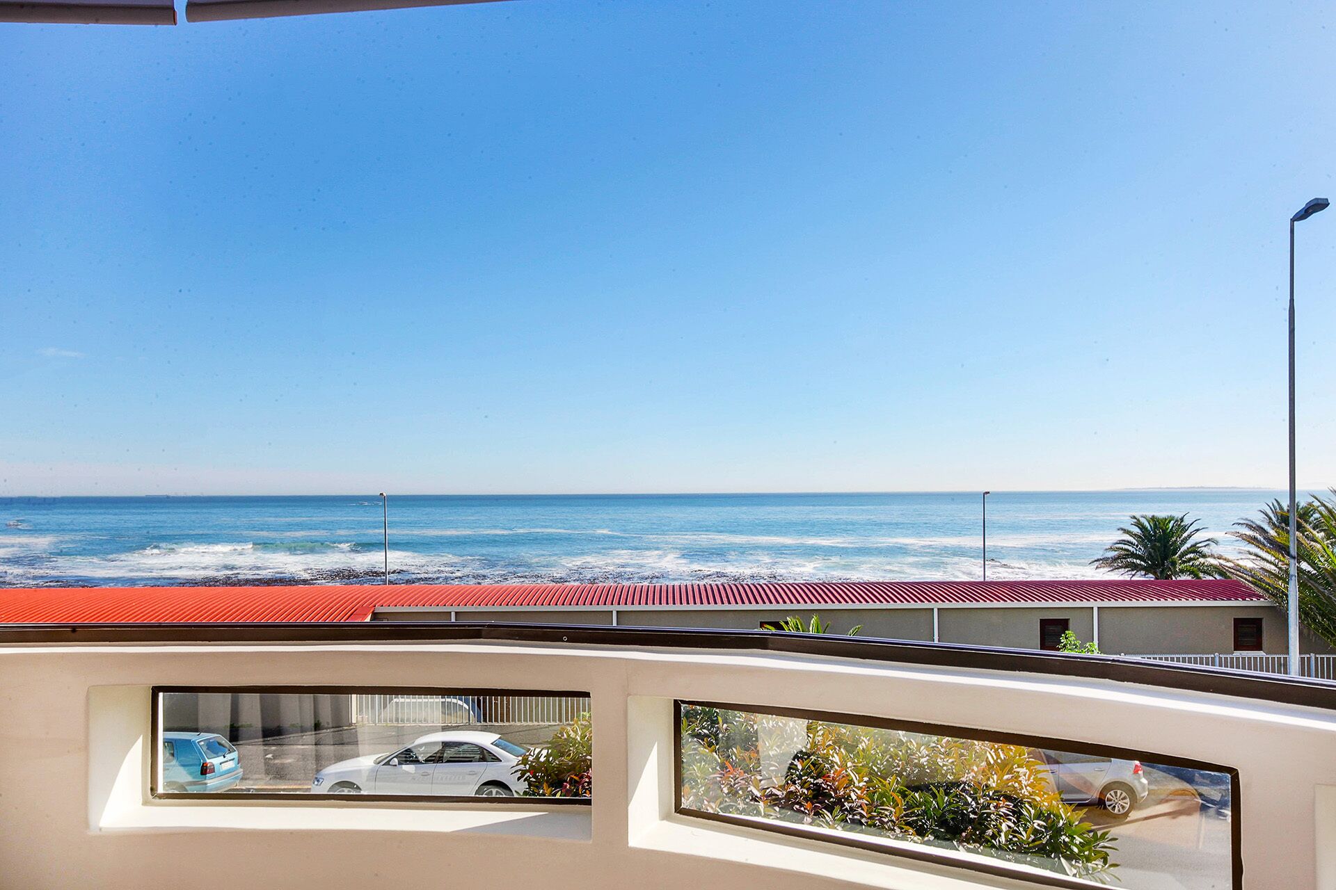 A balcony with a view of the ocean and a red-roofed building.