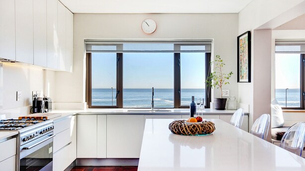 Cocina moderna con una isla grande, vista al océano y un reloj en la pared.