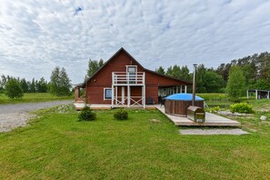 Un chalet rustique avec une façade en bois, un espace extérieur aménagé et couvert, et un petit étang en arrière-plan.