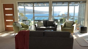 A living room with a sofa, two armchairs, and a view of the sea through large windows. - FIVE BEACHES BEACH HOUSE Bay of Fires (Binalong Bay)