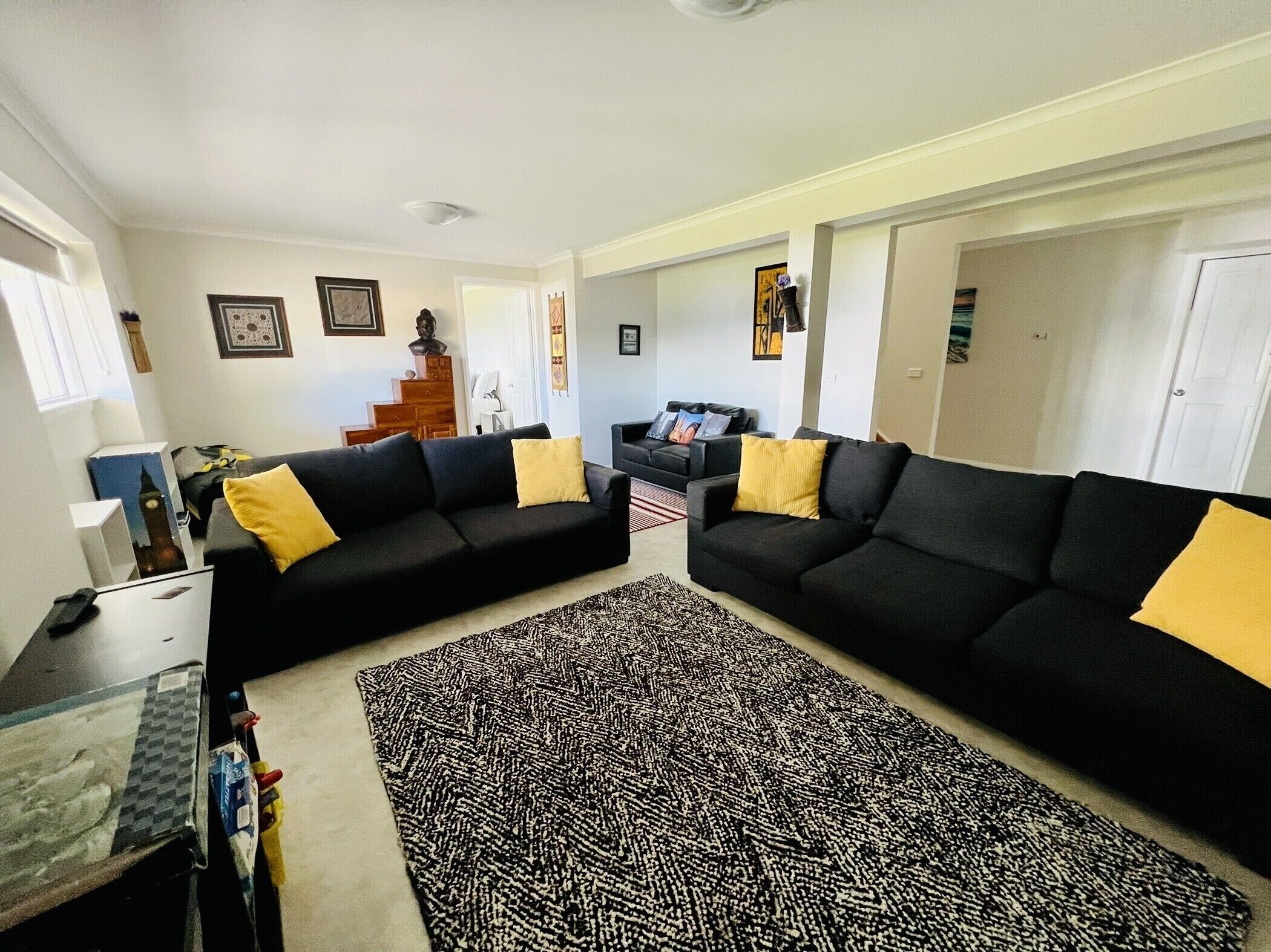 Un salon avec deux canapés noirs, des coussins jaunes, un tapis à motifs et un escalier menant à une autre pièce.