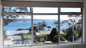 A large window with a view of a coastal landscape, including trees and a body of water. - FIVE BEACHES BEACH HOUSE Bay of Fires (Binalong Bay)