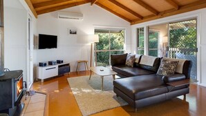 A modern living room with a fireplace, a sofa, a coffee table, and a TV. - Windsong at Ravensbourne Escape 3 Bedrooms (Ravensbourne)