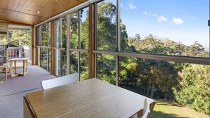A spacious room with large windows offering a view of a forested area. - Windsong at Ravensbourne Escape 3 Bedrooms (Ravensbourne)