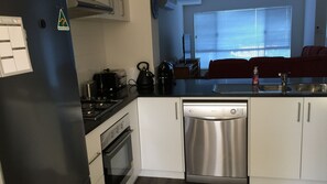 Kitchen features a gas stove, kettle, toaster, and dishwasher, with a modern faucet and adjacent living area.