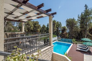 Ein Poolbereich mit Pergola, Sitzmöbeln und Liegestühlen.