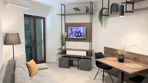 A modern living room with a grey sofa, a wooden dining table, and a TV mounted on the wall. - Standard One-Bedroom Apartment With Balcony And Swimming Pool (Trogir)