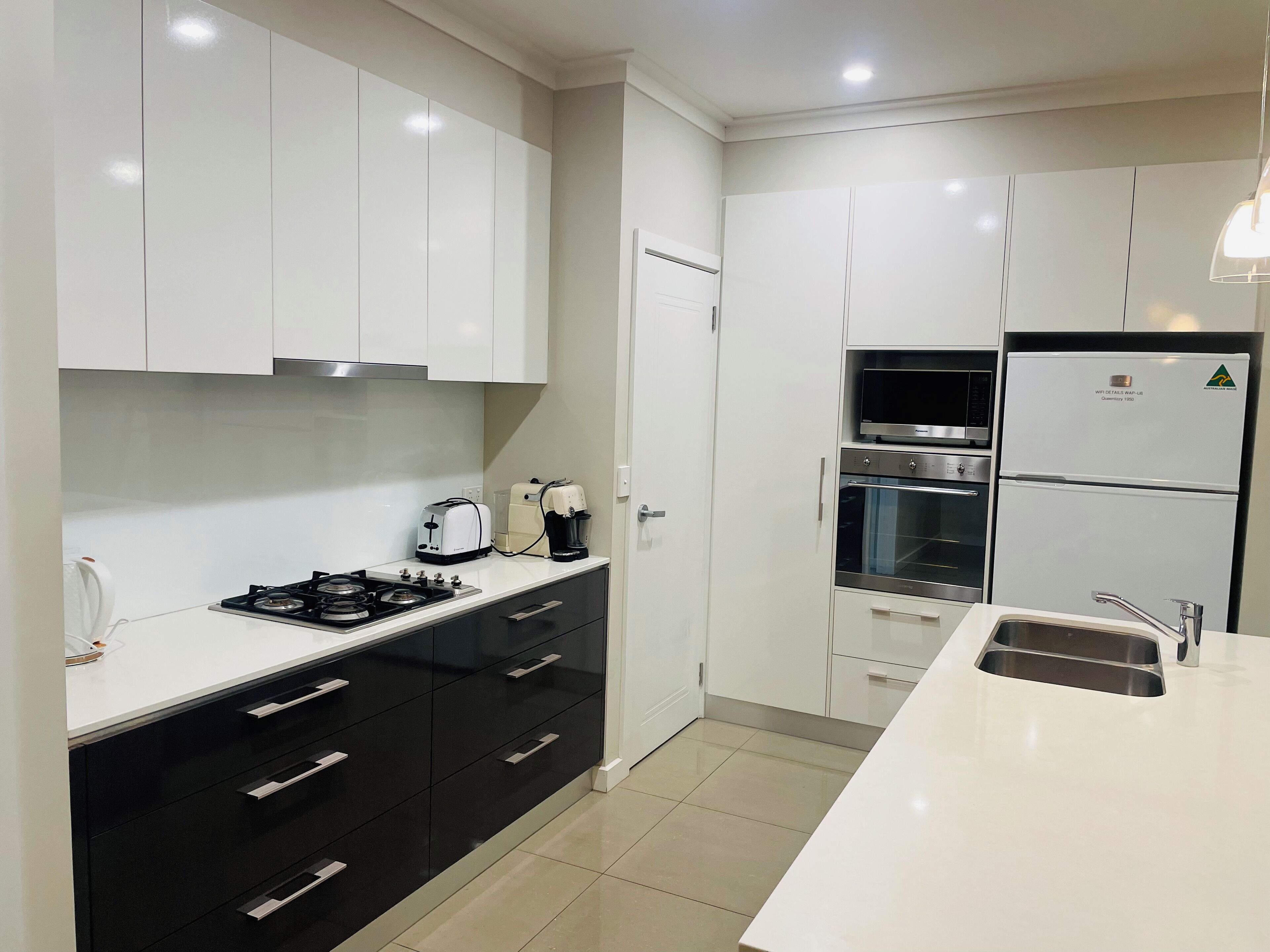 Una cocina moderna con gabinetes blancos, estufa, lavamanos y refrigerador.