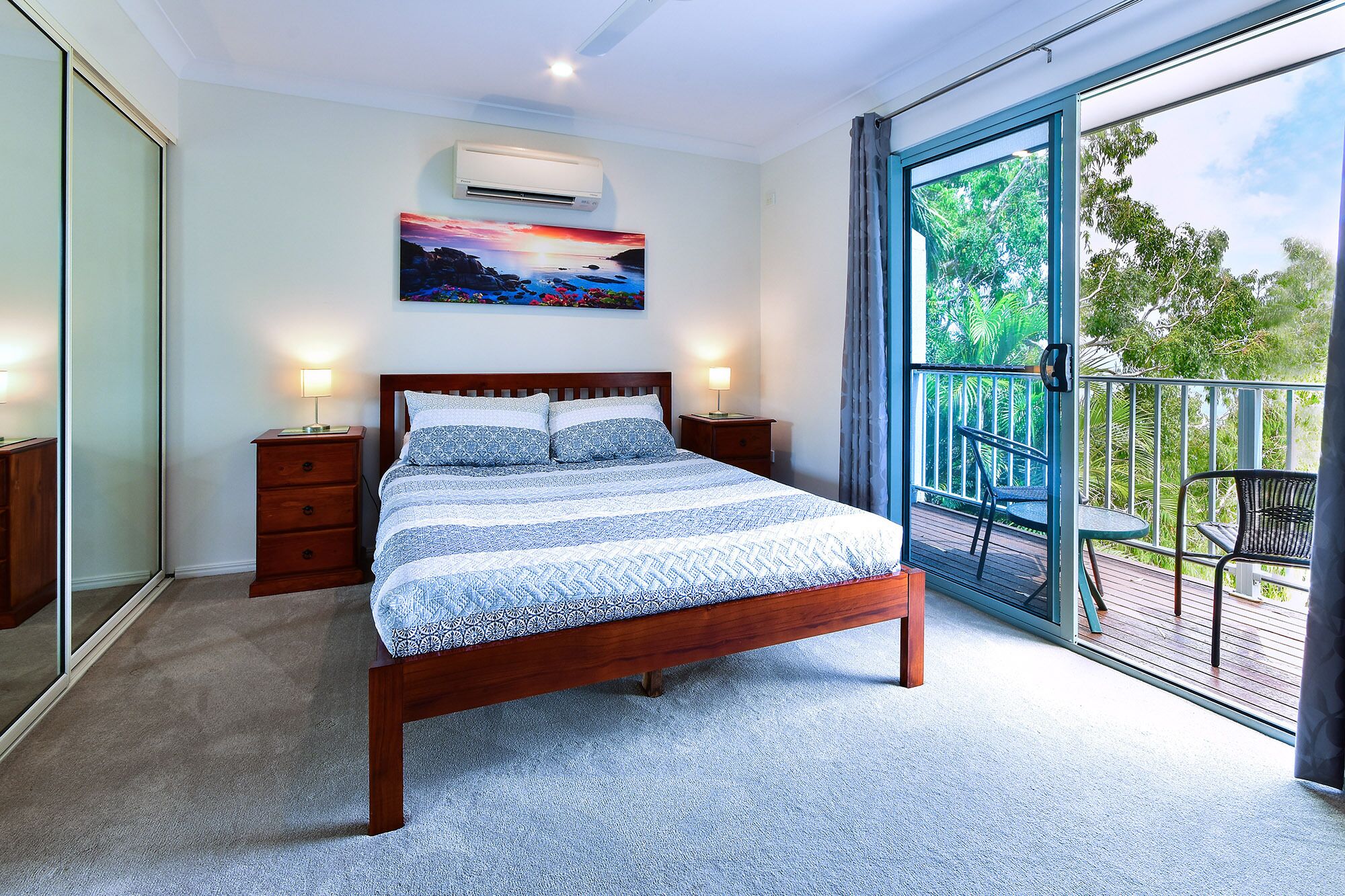 A bedroom with a large bed, a nightstand, a dresser, and a sliding glass door leading to an outdoor balcony.