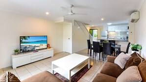 Een moderne woonkamer met een flatscreen televisie, een witte salontafel en een bruine bank.