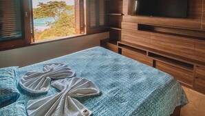 Une chambre à coucher comprenant un lit, un ventilateur de plafond, une télévision et une fenêtre donnant sur des arbres et une étendue d’eau.