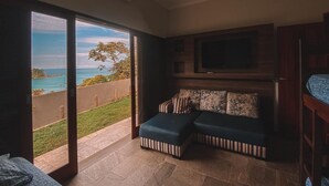 Un salon moderne doté d’un grand téléviseur, d’un canapé d’angle et d’une porte-fenêtre coulissante donnant sur un balcon avec vue sur la mer.