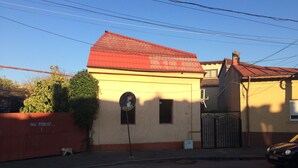 Un petit bâtiment avec un toit rouge et une façade beige, une petite fenêtre et une enseigne sur le mur.