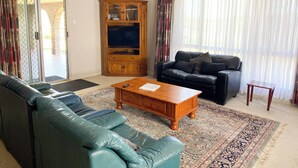 A living room with a green sofa, a wooden coffee table, a black leather couch, and a wooden cabinet with glass doors. - Lancelin Beach house (Lancelin)