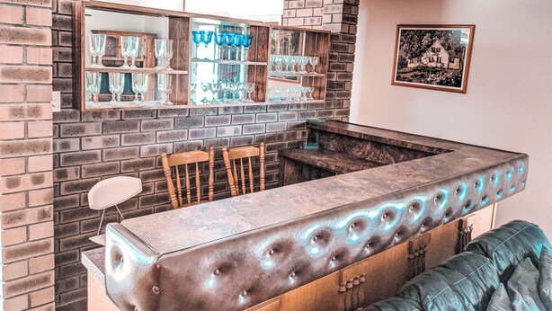 A bar area with a brick wall, shelves with glasses, and a cushioned seating area. - Lancelin Beach house (Lancelin)