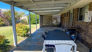 A covered patio with a table and chairs, a brick wall, and a window with a thermostat. - Lancelin Beach house (Lancelin)