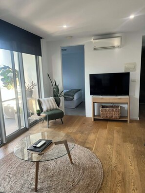 Ein modernes Wohnzimmer mit einem Glastisch, einer Couch, einem Flachbildfernseher und einem großen Fenster.