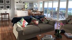 A spacious living room with a large window, a kitchen in the background, and a balcony with a view.