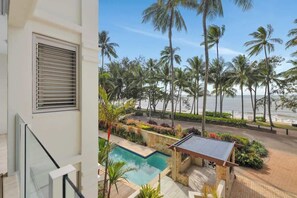 A modern building with a pool, palm trees, and a view of the beach.