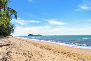 A beach with clear skies, calm sea, and distant islands.