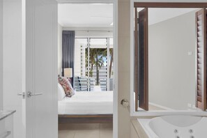 A hotel room with a bed, a window with curtains, a view of palm trees, and a bathtub.