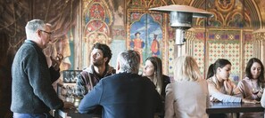 Un groupe de personnes se trouve dans une pièce dont les murs sont décorés dans un style médiéval et qui est illuminée par un grand et somptueux lustre.