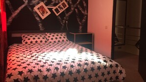 Un dormitorio con una cama y un edredón estampado con motivos de estrellas, un aire acondicionado de pared y dos cuadros enmarcados.