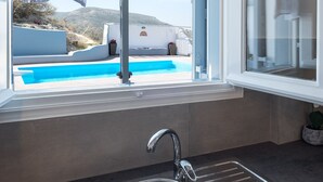 Ett modernt kök med en diskho i rostfritt stål, ett fönster med utsikt över en pool och berg, samt en pergola.