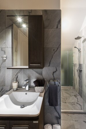 Une salle de bain moderne avec un grand lavabo, des murs en marbre foncé, un miroir et un espace douche.