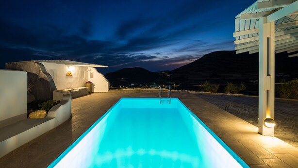En swimmingpool med fri utsikt över det omgivande landskapet, inklusive berg och en modern arkitektonisk byggnad.