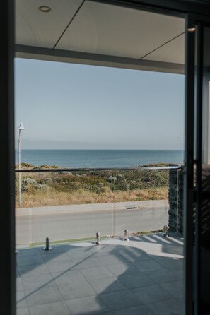 Une vue depuis un balcon donnant sur la mer, avec un ciel dégagé et un horizon lointain.